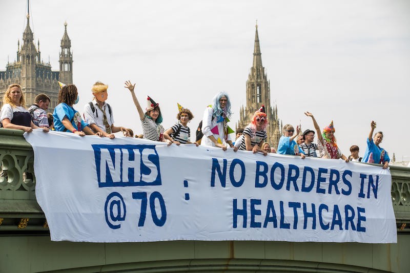People holding banner on bridge: No Borders in Healthcare