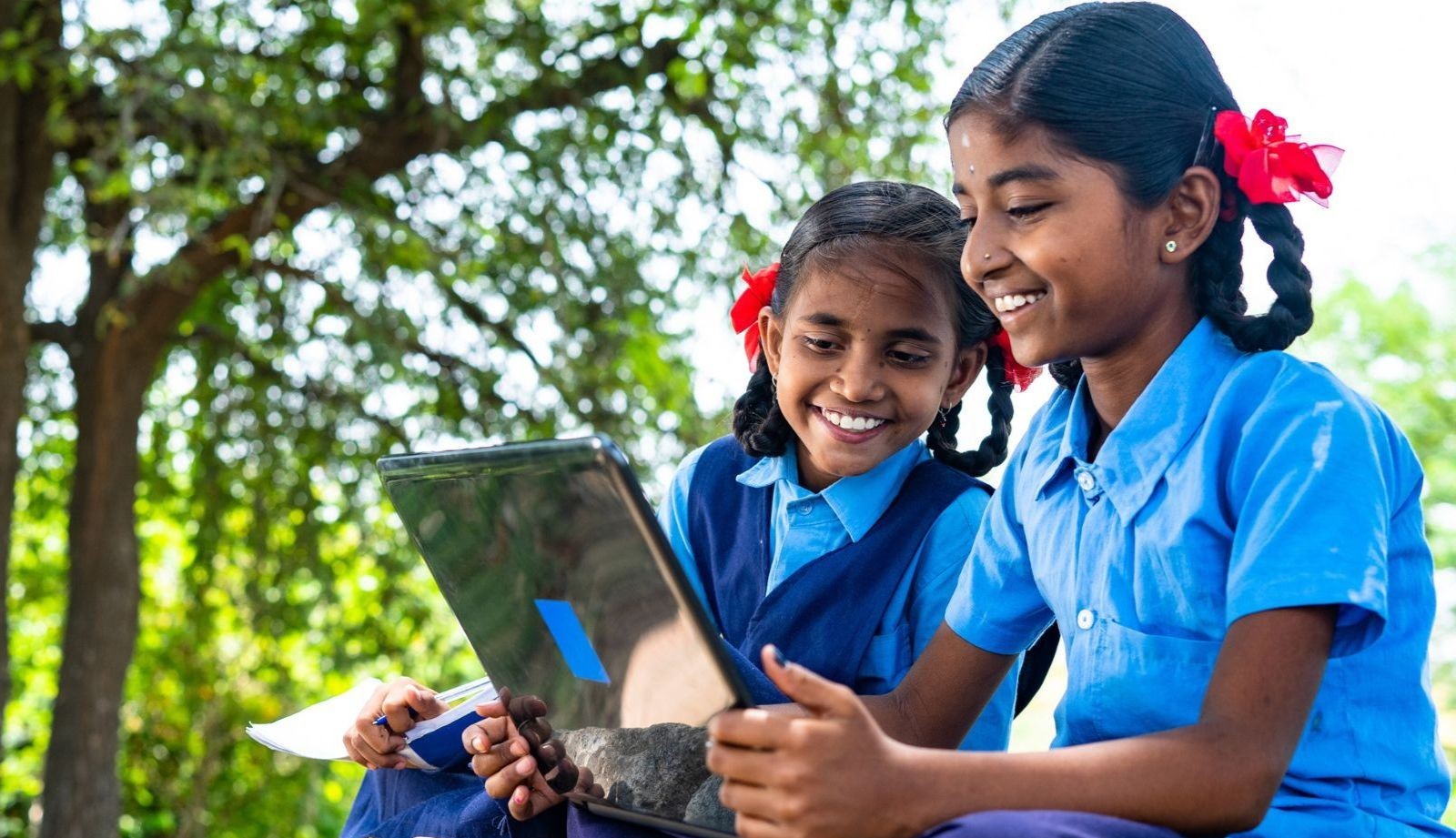 two young girls smile while looking at a tablet