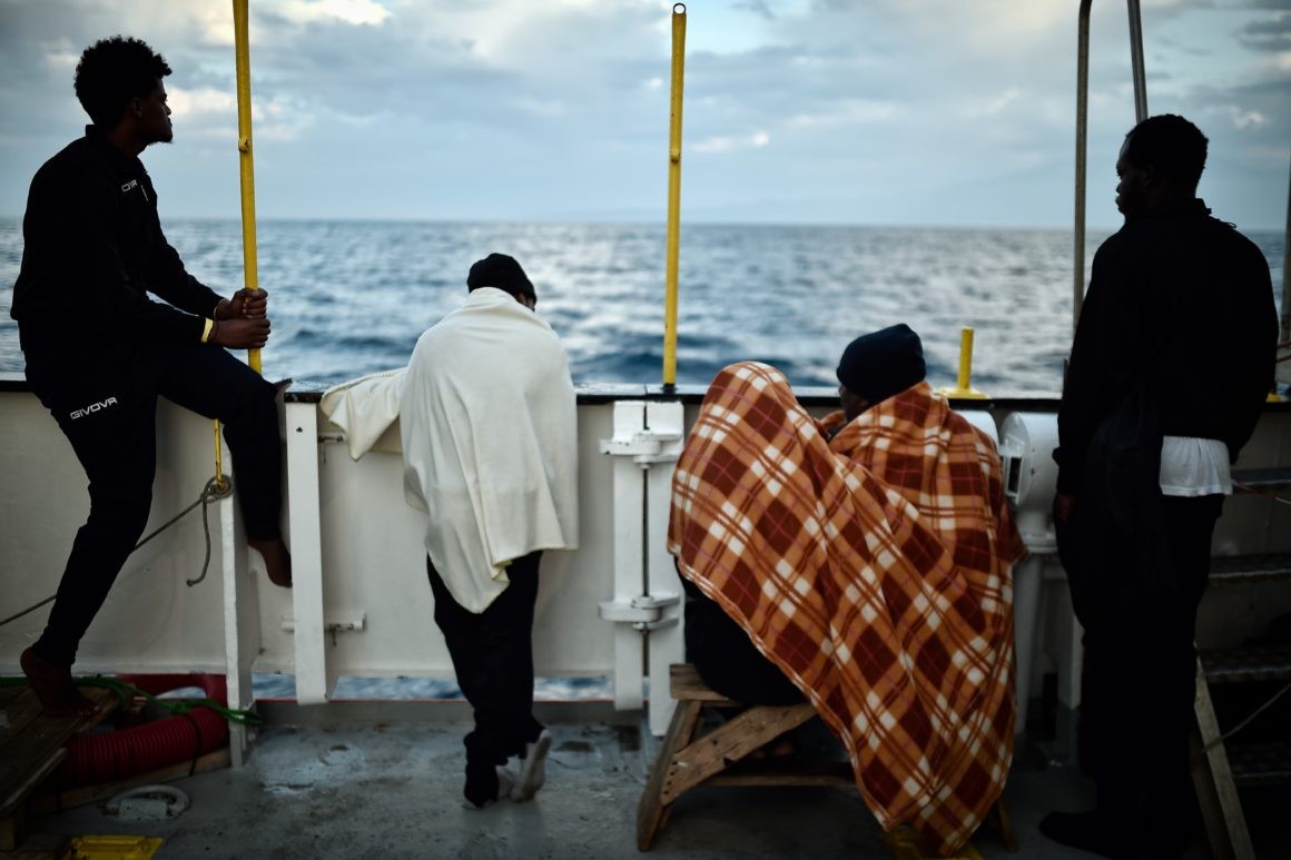 Saved migrants look at the coastline as they stand aboard the rescue ship MV Aquarius off the coast of Sicily in May | Louisa Gouliamaki/AFP via Getty Images