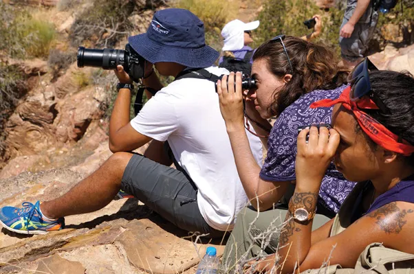students on research field trip looking through binoculars in the wilderness